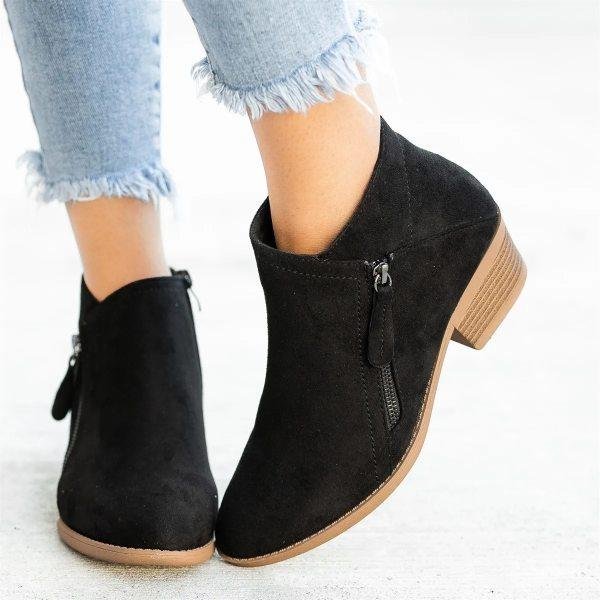 Black suede ankle boots with side zippers, worn with frayed hem jeans. Stylish women's footwear, comfortable design, perfect for casual outfits.