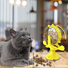 Gray cat with yellow interactive treat dispenser toy on wooden table, blurred background. Cat toy, pet enrichment, feline playtime.