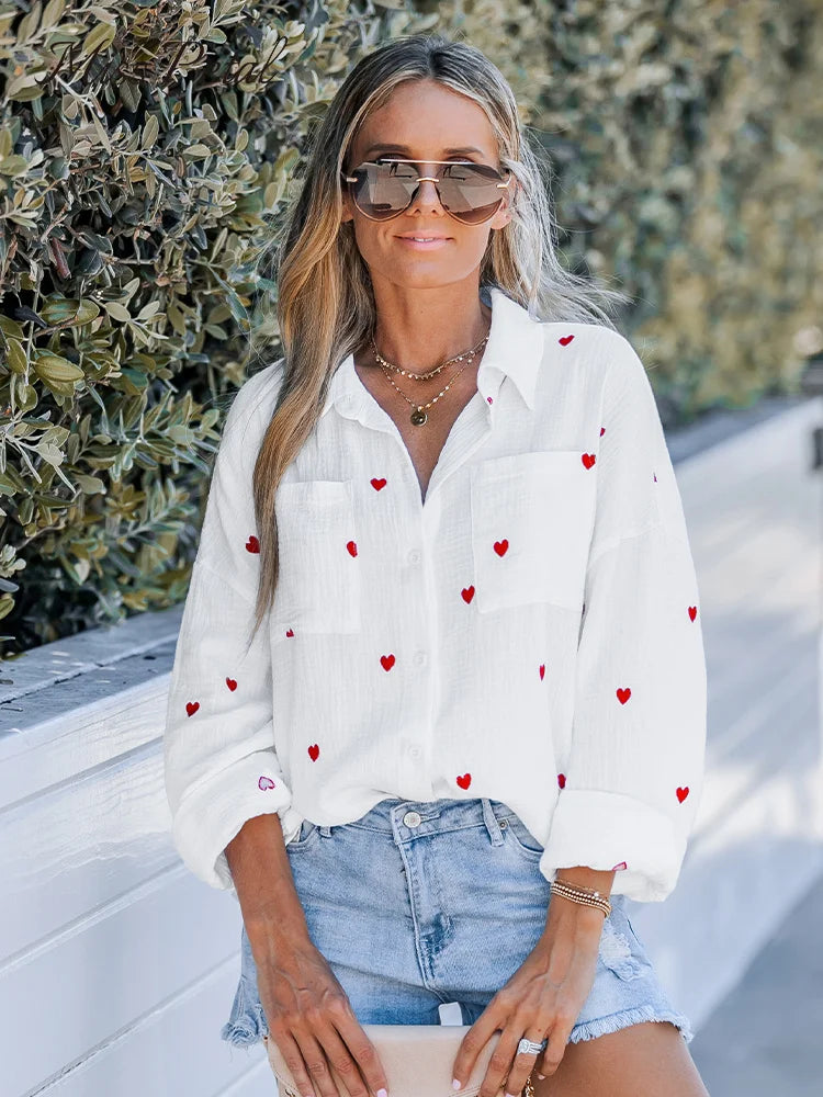 Woman wearing a white cotton embroidered heart crinkle woven shirt, casual loose long sleeve, paired with denim shorts, outdoors.