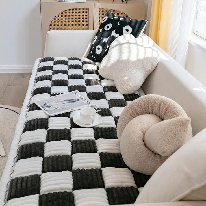 Cream-colored plaid pet mat on a couch, featuring a checkered pattern. Includes decorative pillows and a magazine, perfect for cozy home decor.