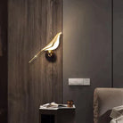 Gold bird-shaped LED wall lamp on dark wood panel, modern lighting fixture for living room or bedroom decor, elegant and stylish home accessory.