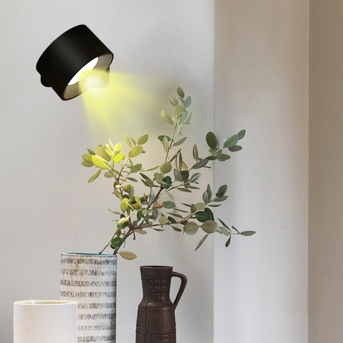 Modern black wall lamp illuminating green plant in stylish ceramic vase, minimalist home decor, contemporary interior design, soft lighting.