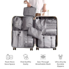 Person holding open suitcase with organized gray packing cubes, featuring see-through mesh and durable zippers. Ideal for efficient travel packing.