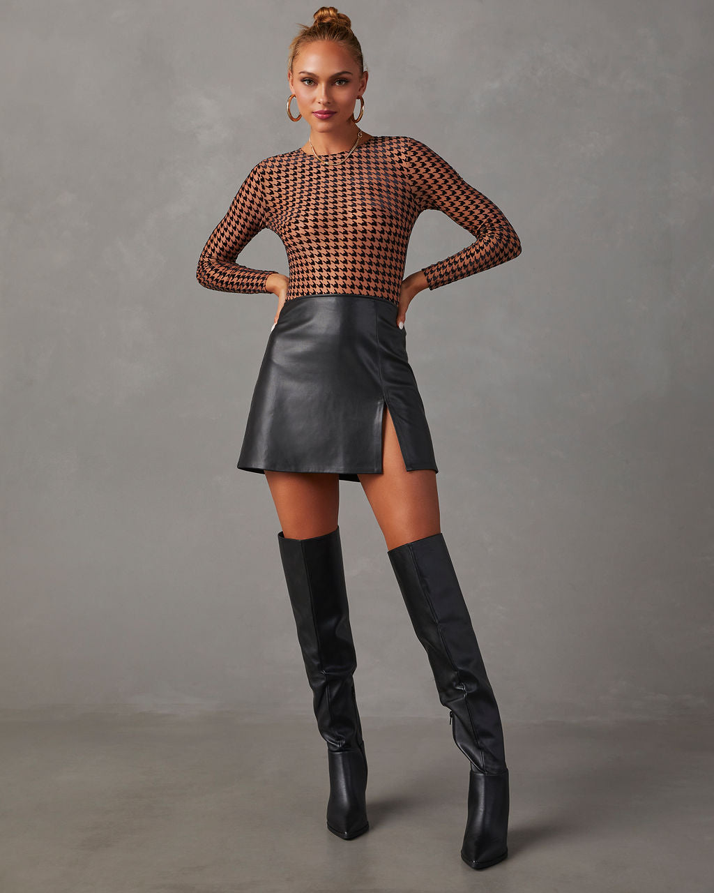 Woman in black leather mini skirt, fishnet top, and knee-high boots, posing confidently. Fashionable outfit, modern style, chic clothing.