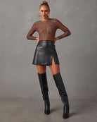 Woman in black leather mini skirt, fishnet top, and knee-high boots, posing confidently. Fashionable outfit, modern style, chic clothing.