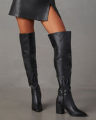 Black knee-high leather boots with block heels, worn with a black skirt. Fashionable women's footwear, perfect for fall and winter style.