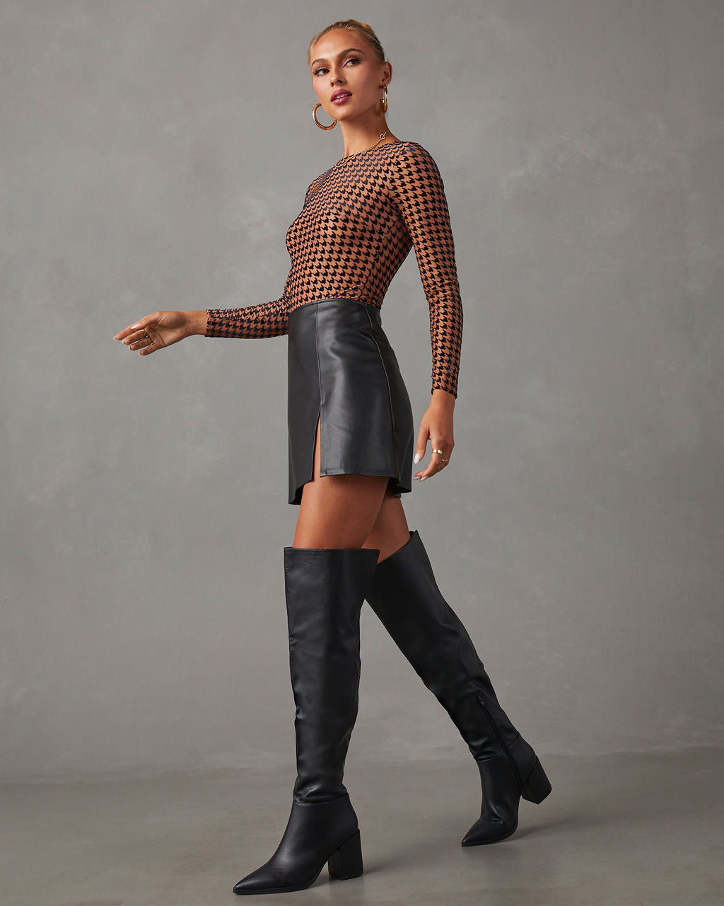 Fashionable woman in black leather mini skirt, houndstooth top, and knee-high boots. Trendy fall outfit, chic style, modern women's fashion.