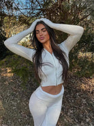 Woman in a white two-piece knit set with long sleeves and zipper hoodie, posing outdoors. Fashionable women's loungewear, stylish outfit.