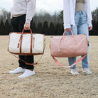 Two people holding stylish, spacious folding duffel bags in beige and pink, perfect for travel and gym use, featuring leather accents and adjustable straps.