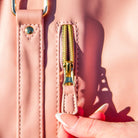 Close-up of a pink folding duffel bag with a gold zipper and a hand holding the strap. Stylish travel accessory, durable material, elegant design.