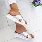 Silver cross-strap sandals with white soles on a woman's feet, stylish summer footwear, modern design, perfect for casual wear.