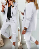 Woman in stylish white blazer and pants set, holding a smartphone. Fashionable casual outfit with black top and sneakers. Trendy women's clothing.