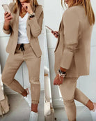 Woman in stylish beige blazer and pants set, white sneakers, and white top, holding a smartphone. Fashionable casual outfit for women.