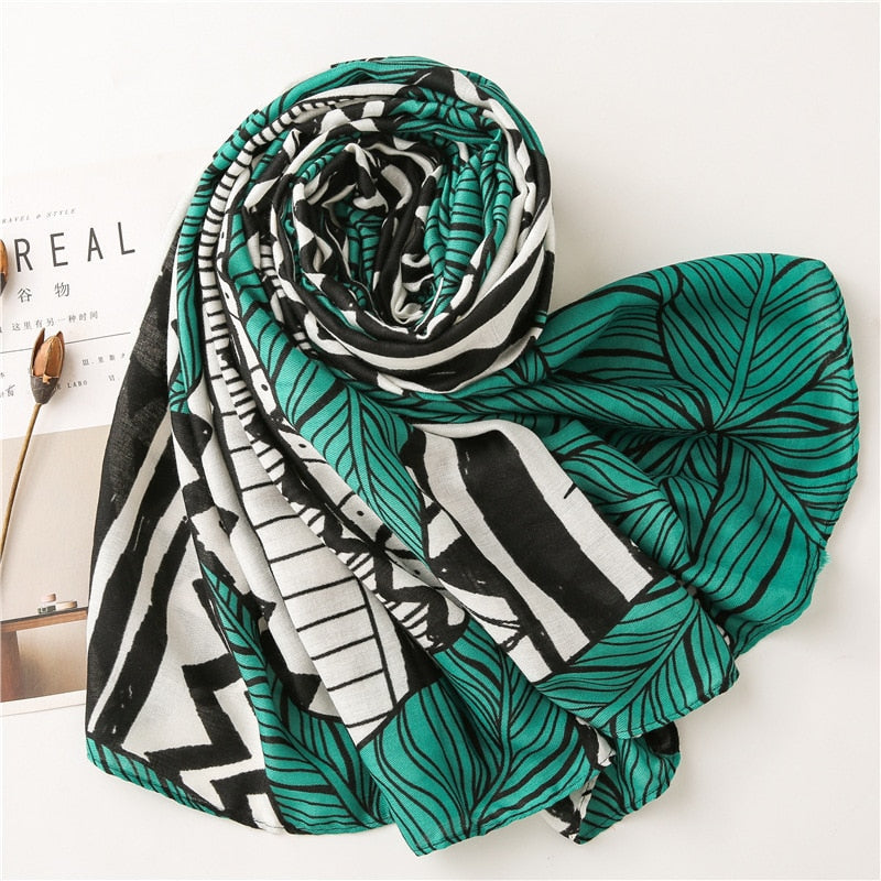 Green and black leaf-patterned scarf on white background, featuring bold geometric designs. Fashion accessory, stylish women's scarf, modern print.