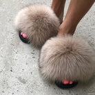 Fluffy fur slippers on feet with pink toenails, stylish footwear on concrete floor. Cozy, fashionable, plush slides for indoor comfort.