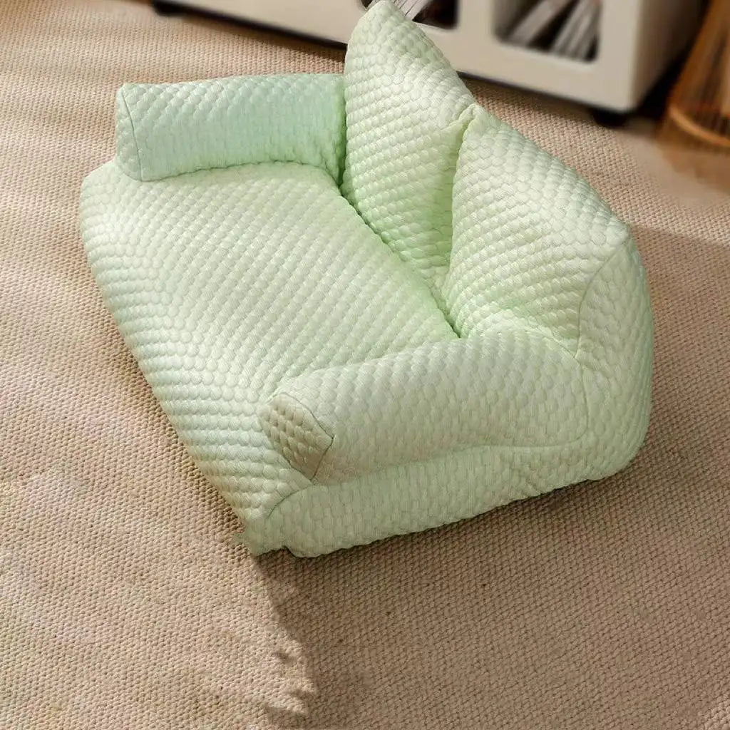 Light green textured pet sofa bed on beige carpet, featuring a quilted design and raised sides for comfort. Ideal for small dogs or cats.