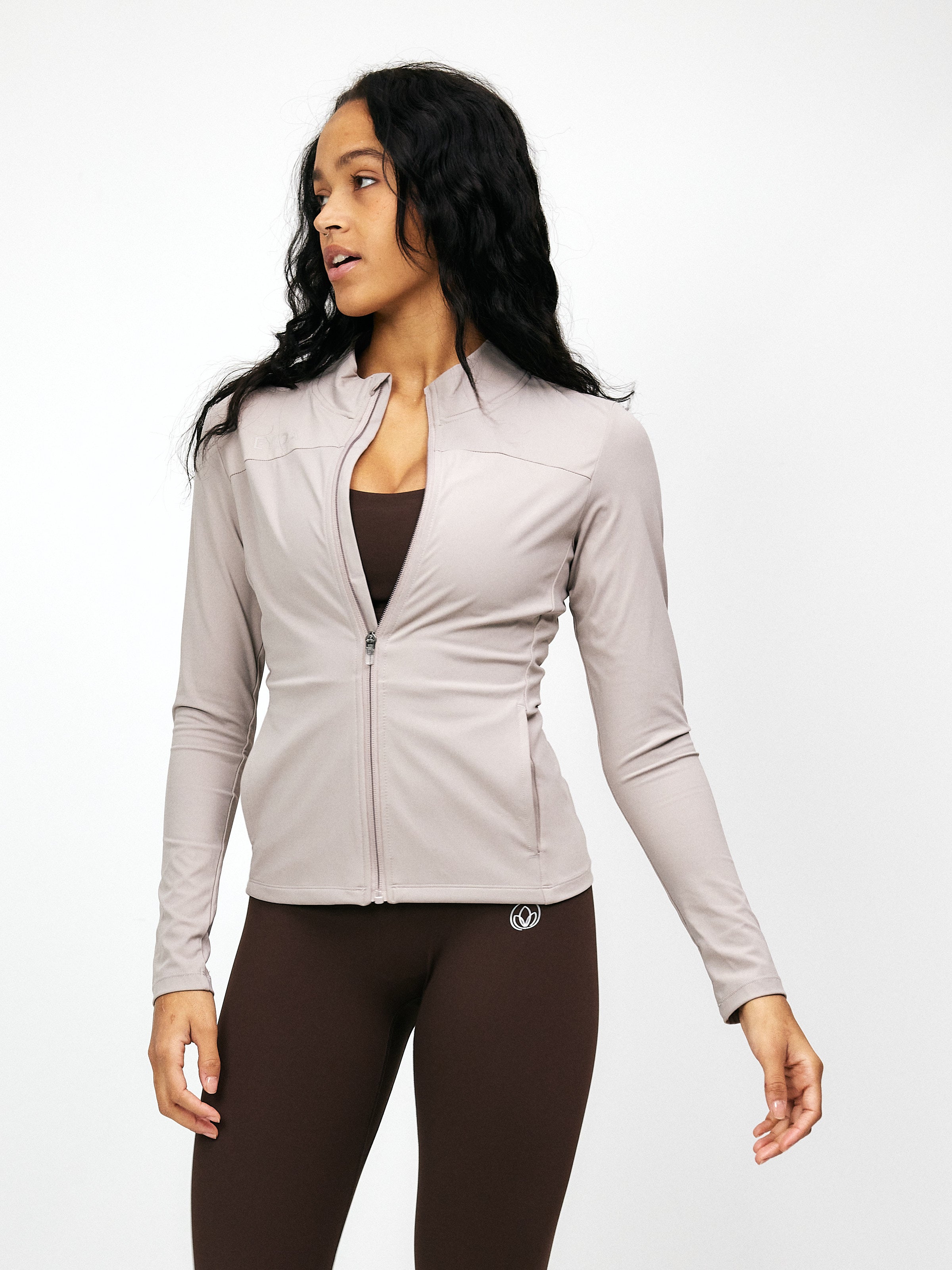 Woman wearing taupe zip-up blouse and brown leggings, showcasing stylish activewear. Perfect for fitness, yoga, or casual outings. Fashionable and comfortable.