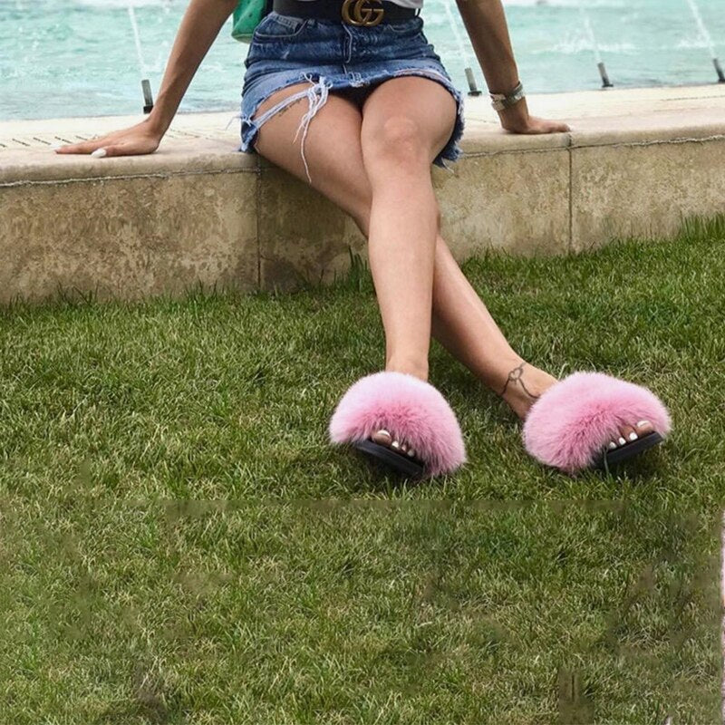 Woman sitting by a pool wearing pink fluffy slippers and a denim skirt. Fashionable summer footwear, casual outdoor style, trendy accessories.