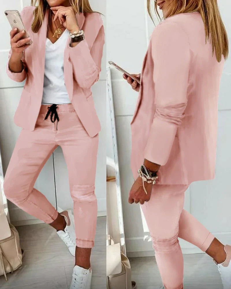 Woman in stylish pink blazer and pants set, holding a smartphone. Fashionable casual outfit with white sneakers and accessories. Trendy women's fashion.