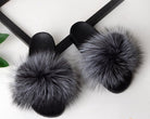 Black faux fur slides with fluffy grey pom-poms, stylish indoor slippers, cozy footwear for women, luxury home fashion, comfortable slip-ons.