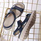 Navy blue orthopedic sandals with adjustable straps and cushioned soles on a gold wire chair, ideal for comfort and support.