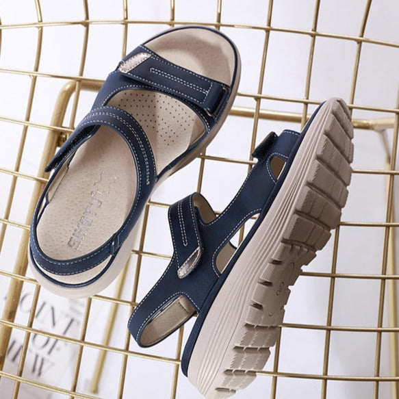 Navy blue orthopedic sandals with adjustable straps and cushioned soles on a gold wire chair, ideal for comfort and support.