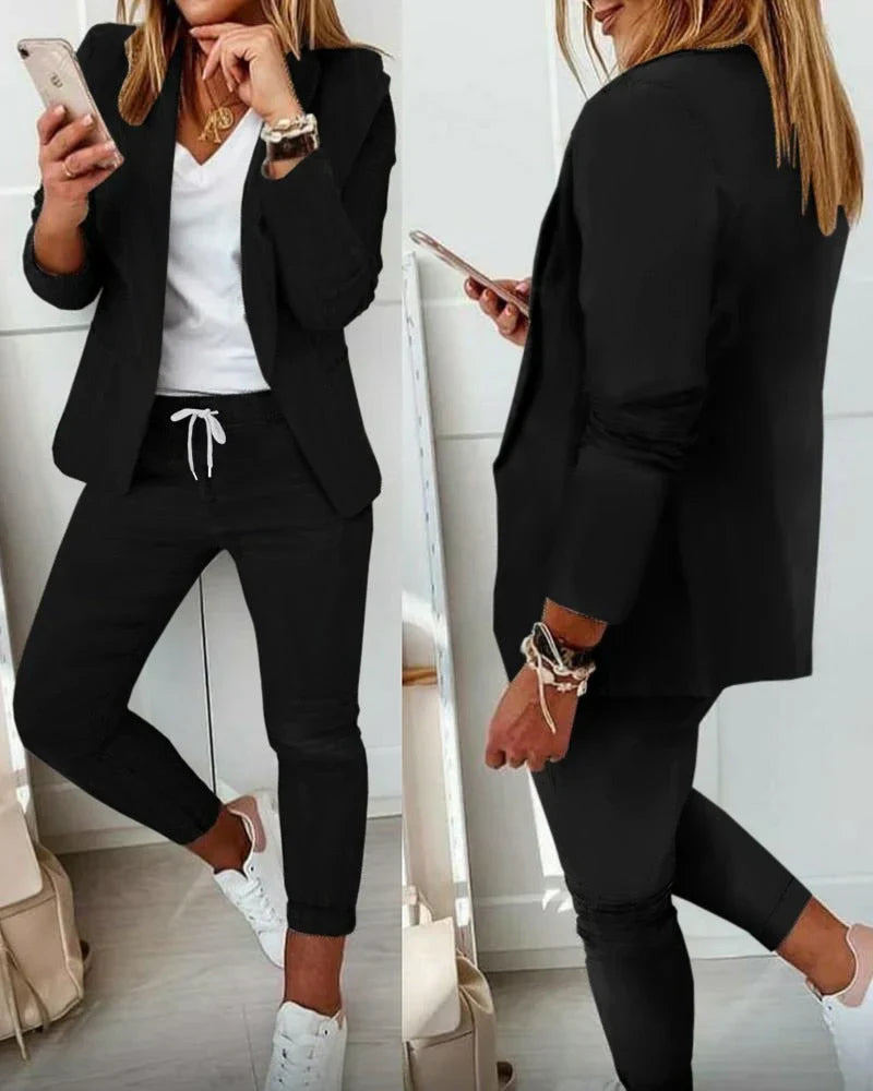 Woman in stylish black blazer and jogger pants set, holding a smartphone. Casual chic outfit with white sneakers, perfect for modern fashion trends.