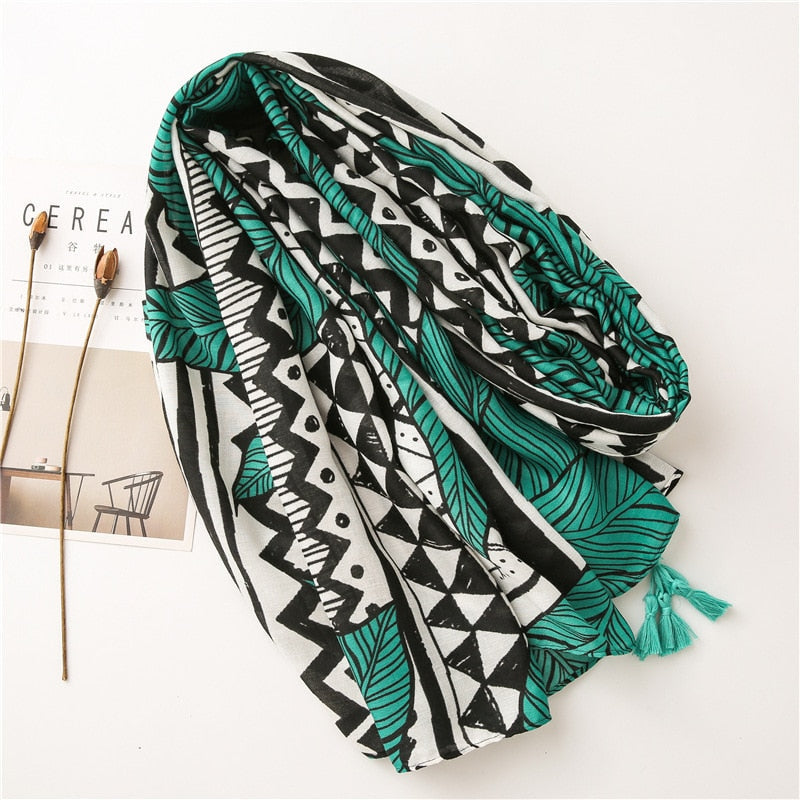 Geometric patterned scarf with green and black tribal design, featuring tassels, displayed on a white surface. Fashion accessory, boho style.