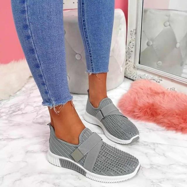 Gray slip-on women's sneakers with Velcro strap, enhancing posture, on marble floor. Fashionable, comfortable footwear for casual wear.