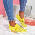 Yellow slip-on sneakers with velcro strap, worn with blue jeans. Stylish women's footwear for improved posture. Perfect for casual wear.