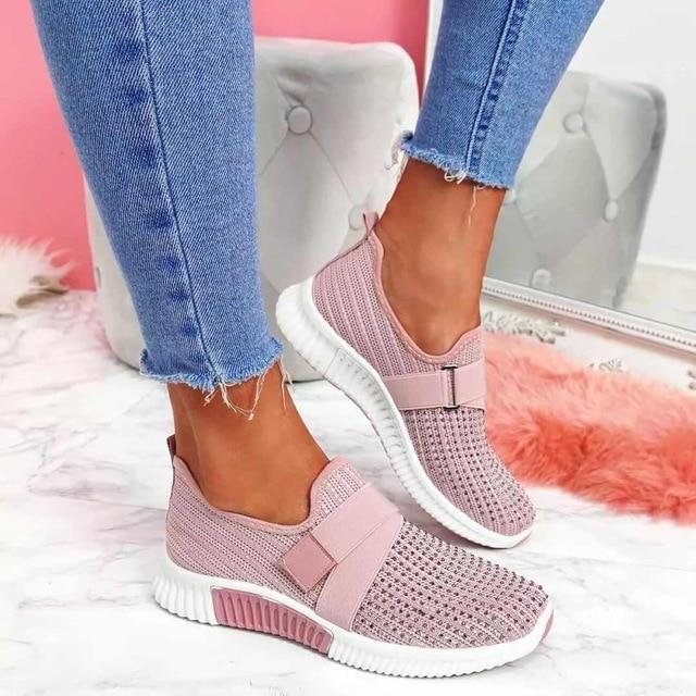 Pink slip-on sneakers with Velcro strap, worn with blue jeans. Stylish women's footwear for improved posture. Comfortable, trendy design.