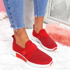 Red slip-on sneakers with Velcro straps, worn with blue jeans, on a stylish background. Comfortable women's footwear for improved posture.