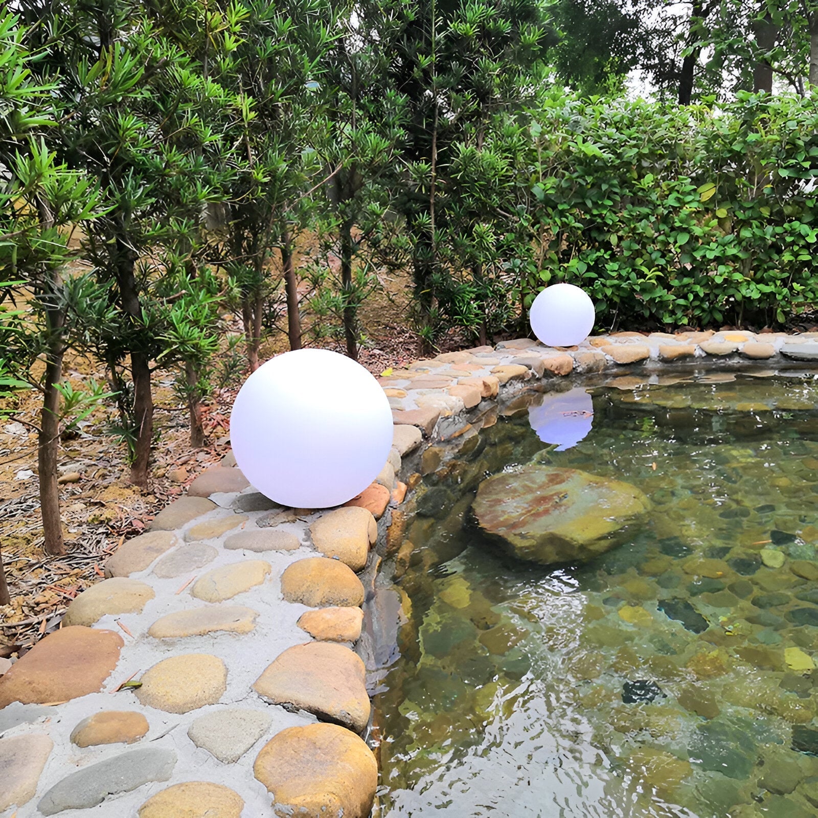 LED Glimmer Sphere lights by a stone-bordered pond, surrounded by lush greenery, ideal for outdoor garden decoration and ambient lighting.