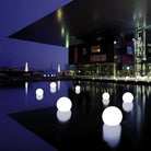 Illuminated LED spheres floating on a reflective water surface at night, creating a modern outdoor decor ambiance with glowing orbs and architectural backdrop.