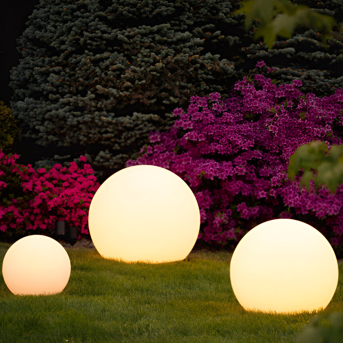 Glowing LED sphere lights in a garden setting with vibrant pink flowers and lush greenery, perfect for outdoor decoration and ambient lighting.