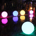 Colorful LED spheres illuminate a rainy outdoor setting, reflecting vibrant hues on wet surfaces. Perfect for garden decoration and ambient lighting.