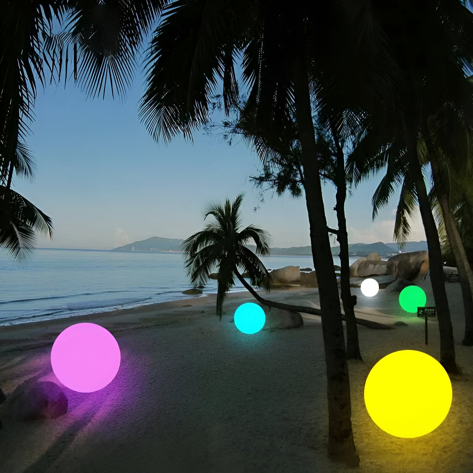 Colorful LED spheres illuminate a tropical beach at dusk, surrounded by palm trees and ocean views. Outdoor decorative lighting, vibrant ambiance.