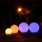 Colorful LED spheres glowing in the dark outdoors, featuring vibrant yellow, orange, blue, and purple lights, ideal for garden decoration.