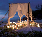 Outdoor beach canopy with glowing LED sphere lights, draped white fabric, and lush greenery, creating a romantic evening ambiance.