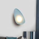 Modern blue pebble-shaped wall light illuminating a contemporary living room, featuring sleek design and soft ambient lighting.