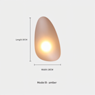 Amber pebble-shaped wall light, Model B, with dimensions 30cm length and 18cm width, emits warm glow. Modern home lighting decor.