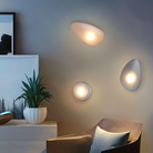 Modern pebble-shaped wall lights illuminating a stylish living room with contemporary decor, featuring a potted plant and abstract art.