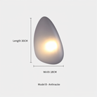 Anthracite pebble-shaped wall light, Model B, 30cm length, 18cm width, emits warm glow. Modern home lighting, minimalist design, interior decor.