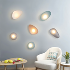 Modern pebble-shaped wall lights in various colors on a gray wall, enhancing contemporary home decor. Stylish lighting design for living rooms.