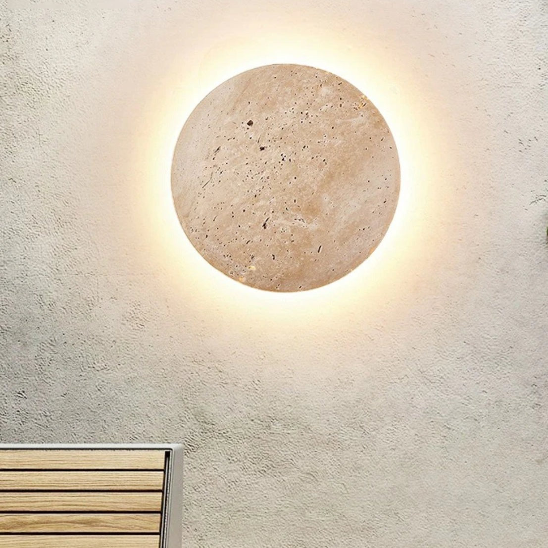 Modern round wall light fixture with a stone finish, emitting a warm glow, mounted on a textured beige wall above a wooden bench. Ideal for home decor.