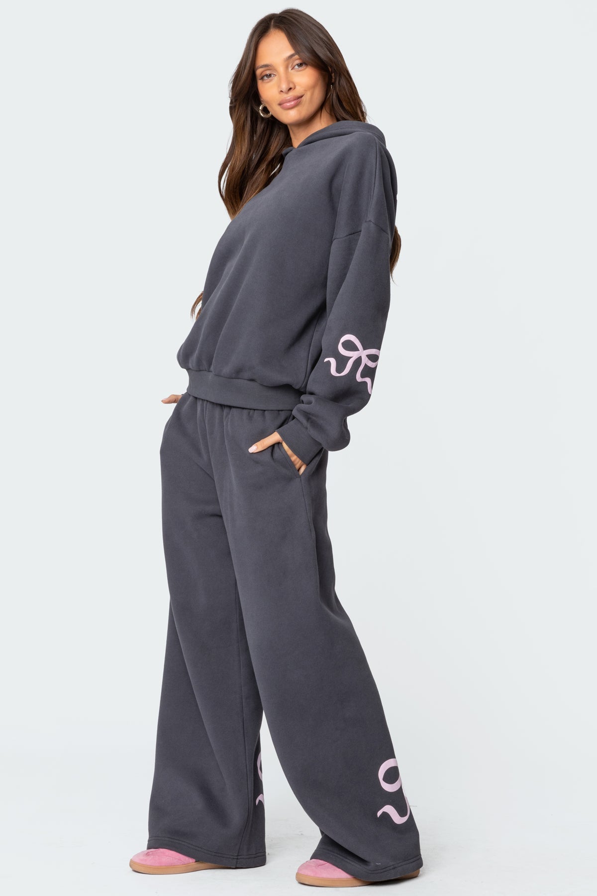 Woman in dark gray oversized hoodie and wide-leg sweatpants with pink accents, standing confidently. Cozy loungewear fashion, casual style.