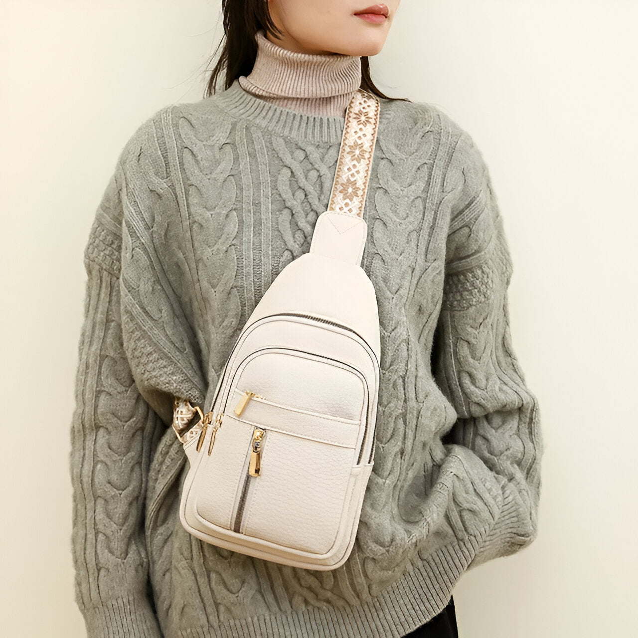 Woman wearing a stylish gray cable knit sweater with a beige crossbody bag featuring gold zippers and a patterned strap, perfect for casual fashion.