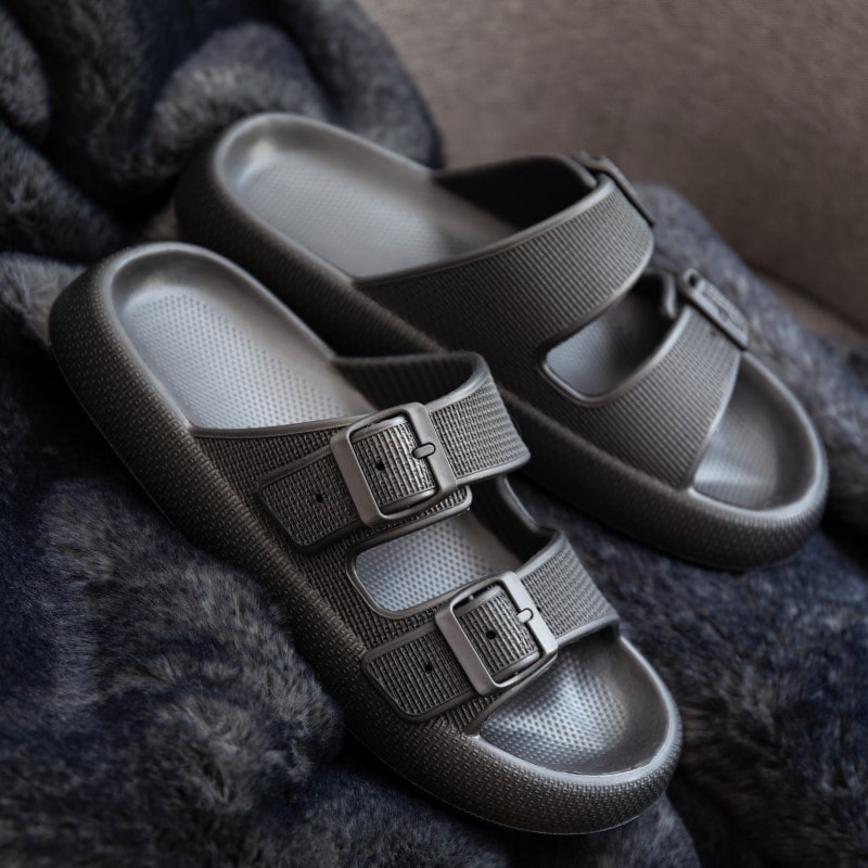 Gray slide sandals with dual adjustable buckles on a plush dark fabric background, showcasing modern casual footwear design and comfort.