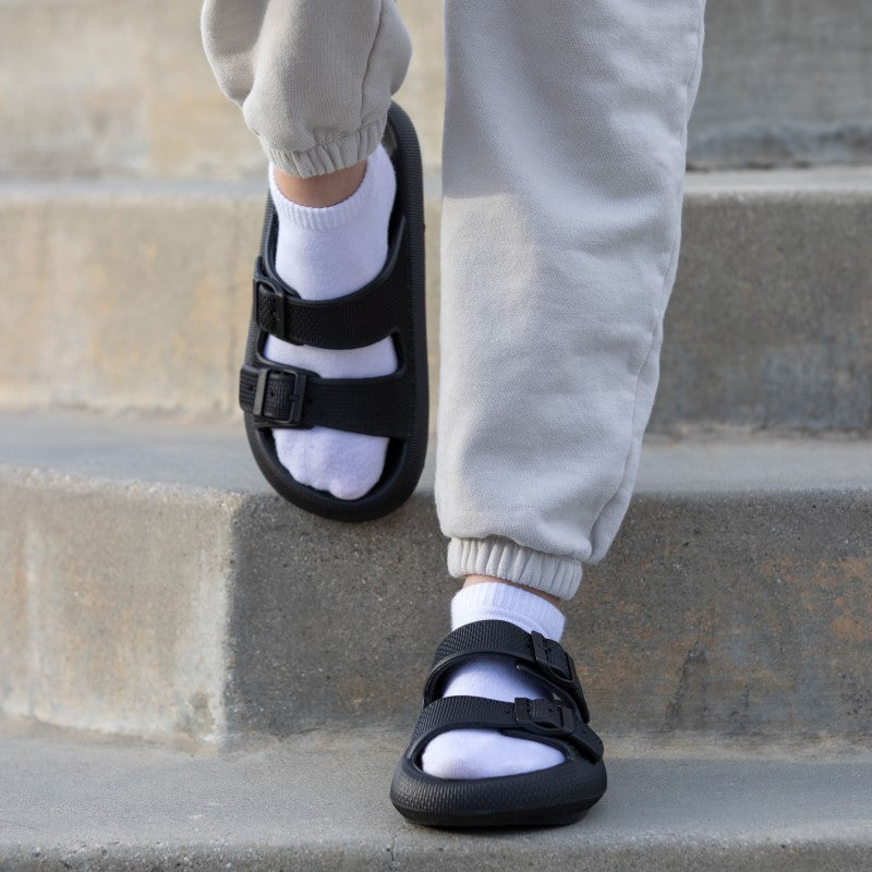 Person wearing black buckle sandals with white socks and gray sweatpants walking down concrete steps. Comfortable casual footwear fashion.