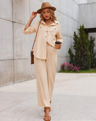 Woman in stylish khaki two-piece outfit with wide-leg pants and button-up shirt, wearing a hat and holding a coffee cup, walking outdoors.